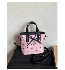 Détail du sac à main rose avec motifs de nœuds noirs et pendentif en forme de cœur argenté