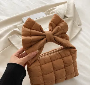 Detail view of the brown quilted handbag with a large decorative bow handle and zip closure