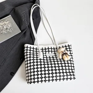 Detail of checkered tote bag with plush bear charm and JINGPIN logo on white surface