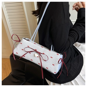 Détail du sac sous le bras avec nœud rouge et pendentif cœur argenté sur modèle