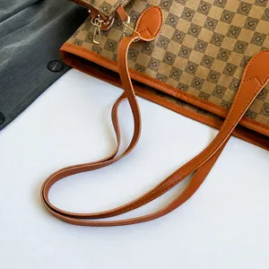 Dettaglio dei manici in pelle di una borsa tote a scacchi marrone con fibbie oro