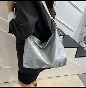 Detail of silver tote bag with crinkle texture and metal hardware on shoulder strap