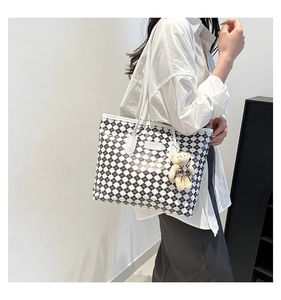 Detail of checkered tote bag featuring a cute teddy bear charm and brand logo patch