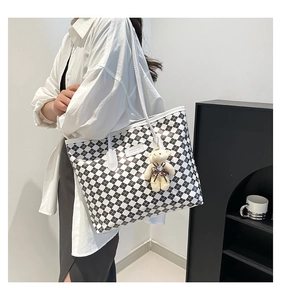 Detail of checkered tote bag on model shoulder with plush bear charm and white straps