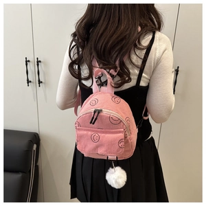 Close-up of pink corduroy mini backpack with black smiley faces and white fuzzy pompom