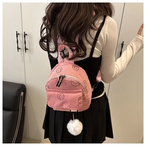 Detail eines rosa Cord-Minirucksacks mit Smiley-Drucken und weißem Bommelanhänger