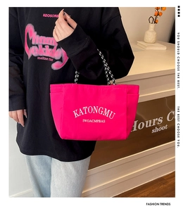 Detail of a bright pink nylon tote bag with white lettering and braided rope handles