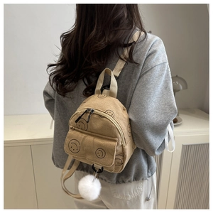 Close-up of khaki corduroy mini backpack featuring a smile print and white pompom charm