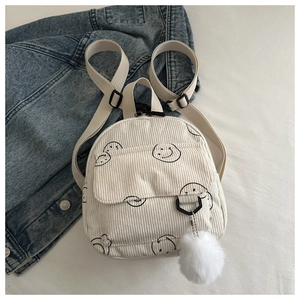 Detail shot of white corduroy mini backpack with smiley pattern and plush pendant