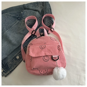 Detail of pink corduroy mini backpack with smiling face print and white fur pompom charm