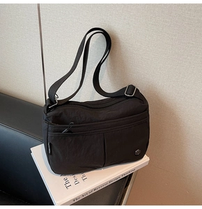 Détail d'un sac bandoulière noir en nylon avec poche zippée et sangle réglable sur un livre
