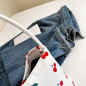 Detail view of red cherry print on white canvas tote bag with reinforced stitching handles
