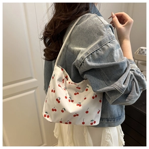 Detail view of white cherry print shoulder bag styled with denim jacket and white dress