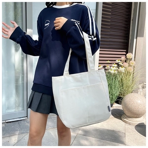 Detailweergave van de witte canvas shopper met groot voorvak en zwart zijlabel aan tas