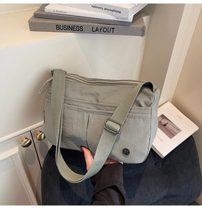 Détail d'un sac bandoulière léger en nylon avec plusieurs poches zippées et logo métallique