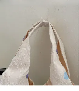 Close-up of beige textured canvas tote handle with light blue and purple floral embroidery