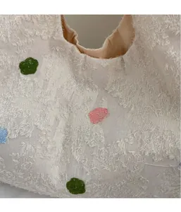 Detailed view of textured cream canvas bag featuring colorful floral embroidery and soft plush fabric