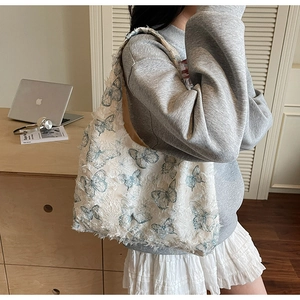 Detail of a beige canvas tote bag featuring intricate blue butterfly embroidery and fringe