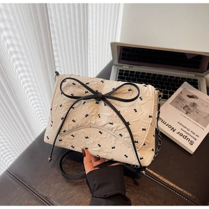 Detail einer weißen gesteppten Handtasche mit Blumenmuster und großer schwarzer Schleife