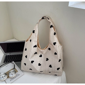 Detail of a beige tote bag with black heart patterns next to a laptop and books