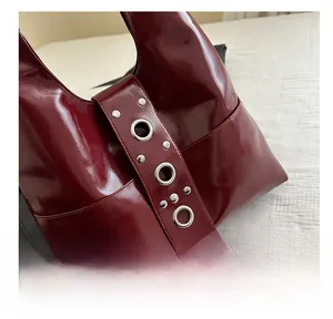 Detalle del bolso tote de charol granate con ojales y remaches de metal plateado