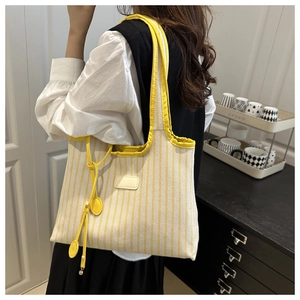 Detailed close-up of yellow striped canvas tote bag with decorative patch and charm