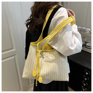 Detail of yellow and white striped tote bag with leather straps on a side-profile model