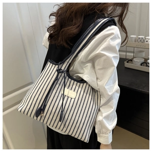 Detail of blue striped tote bag featuring side drawstring with metal beads and tassel