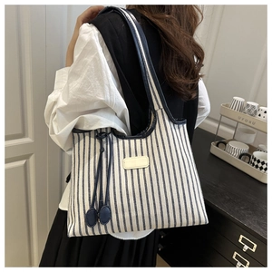 Close-up of a blue and white striped canvas tote bag with tassels and leather patch detail