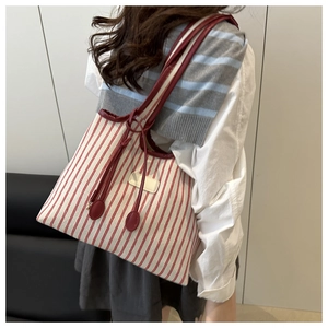 Side view of large striped canvas tote bag with red leather straps and detail charms