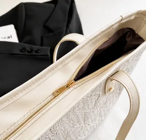 Close-up of smooth gold metal zipper and woven texture on beige faux leather tote bag
