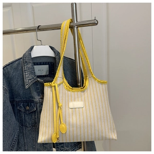 Detail of yellow striped canvas tote bag with hanging tie decor and leather patch
