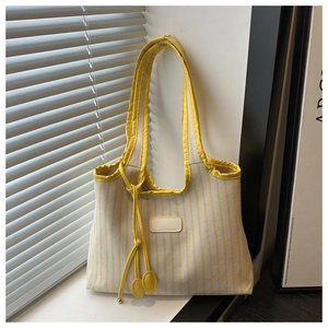Detail of yellow striped canvas tote bag with leather piping and decorative round pendant