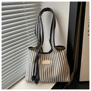 Detail of striped canvas tote bag featuring leather shoulder straps and side drawstring