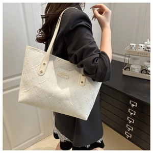 Close-up of white textured tote bag with gold rivets and brand plate on shoulder strap
