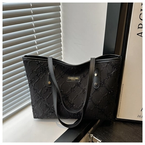 Dettaglio della borsa tote nera testurizzata con logo metallico e raffinati manici in pelle