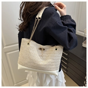 Dettaglio borsa tote in paglia intrecciata con catena dorata, fondo in pelle e ciondolo