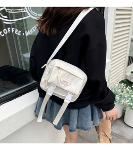 Rear view of a beige nylon crossbody bag with fashion label and white buckle straps