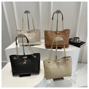 Dettaglio di quattro borse tote in paglia intrecciata con manici a catena dorata e ciondolo