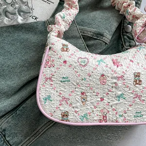 Detail of embossed floral pattern and cute bear print on white quilted fabric underarm bag