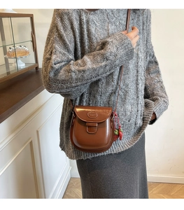 Détail d'un sac besace marron vintage avec un pendentif fraise et logo embossé