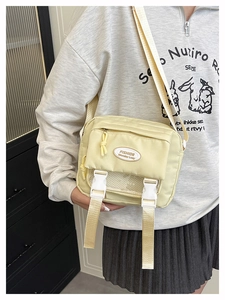 Detail view of cream nylon messenger bag with buckle closure and logo patch