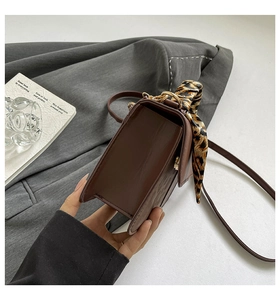 Detail of dark brown leather crossbody bag featuring a leopard print silk scarf accessory