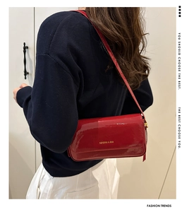 Close-up of red glossy shoulder bag with gold logo lettering on premium leather finish