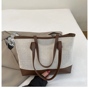 Detail of contrast stitch tote bag featuring cream woven canvas and brown leather trim