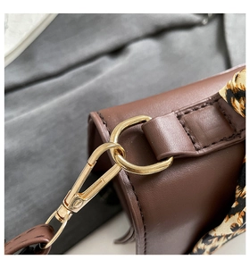 Macro detail of dark brown leather bag with gold hardware and leopard print scarf