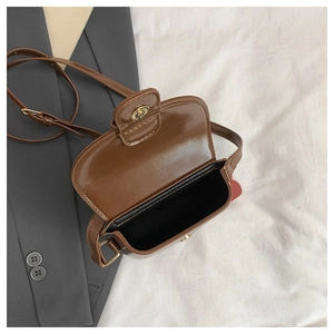 Détail du mini sac bandoulière marron avec boucle magnétique dorée sur blazer gris