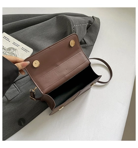 Detailed view of brown crossbody bag with gold magnetic snaps on a textured blazer