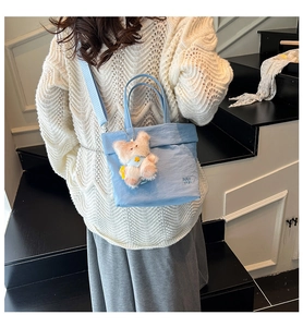 Detail of light blue crossbody bag with bear charm on a model in a knit sweater