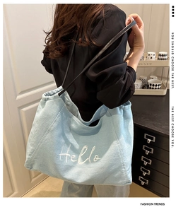 Detail van lichtblauwe denim tote bag met wit Hello borduursel en zwarte leren riemen